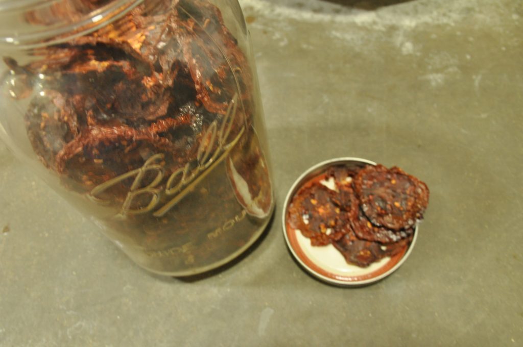 Dried sliced tomatoes in glass jar and lid off to side with tomatoes laying on lid.