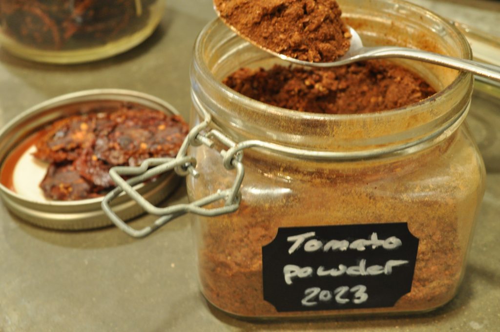 Dried tomato powder in jar with spoon dipping in showing powder up close.