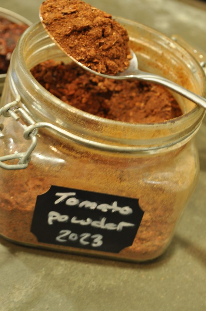 tomato powder displayed on a spoon dipping into a jar full of tomato powder