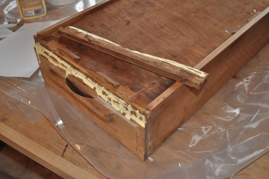 Drawer upside down with wood glue on broken piece and drawer front.